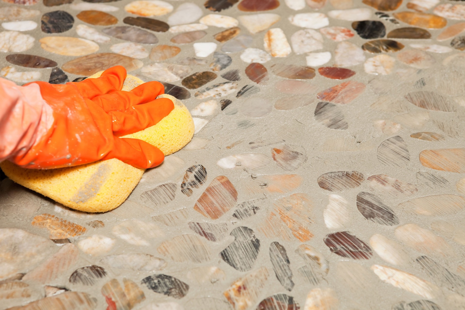 Gloved Hand Using Sponge to Remove Grout from Stone Floor